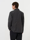 A model is wearing the Charcoal Seattle Cotton OG Bakers Jacket against a plain white background. The image, taken from a side-rear perspective, showcases the jacket's straight hem and the textured charcoal grey cotton fabric. The model's hands are placed in the large lower patch pockets. No other accessories are visible.