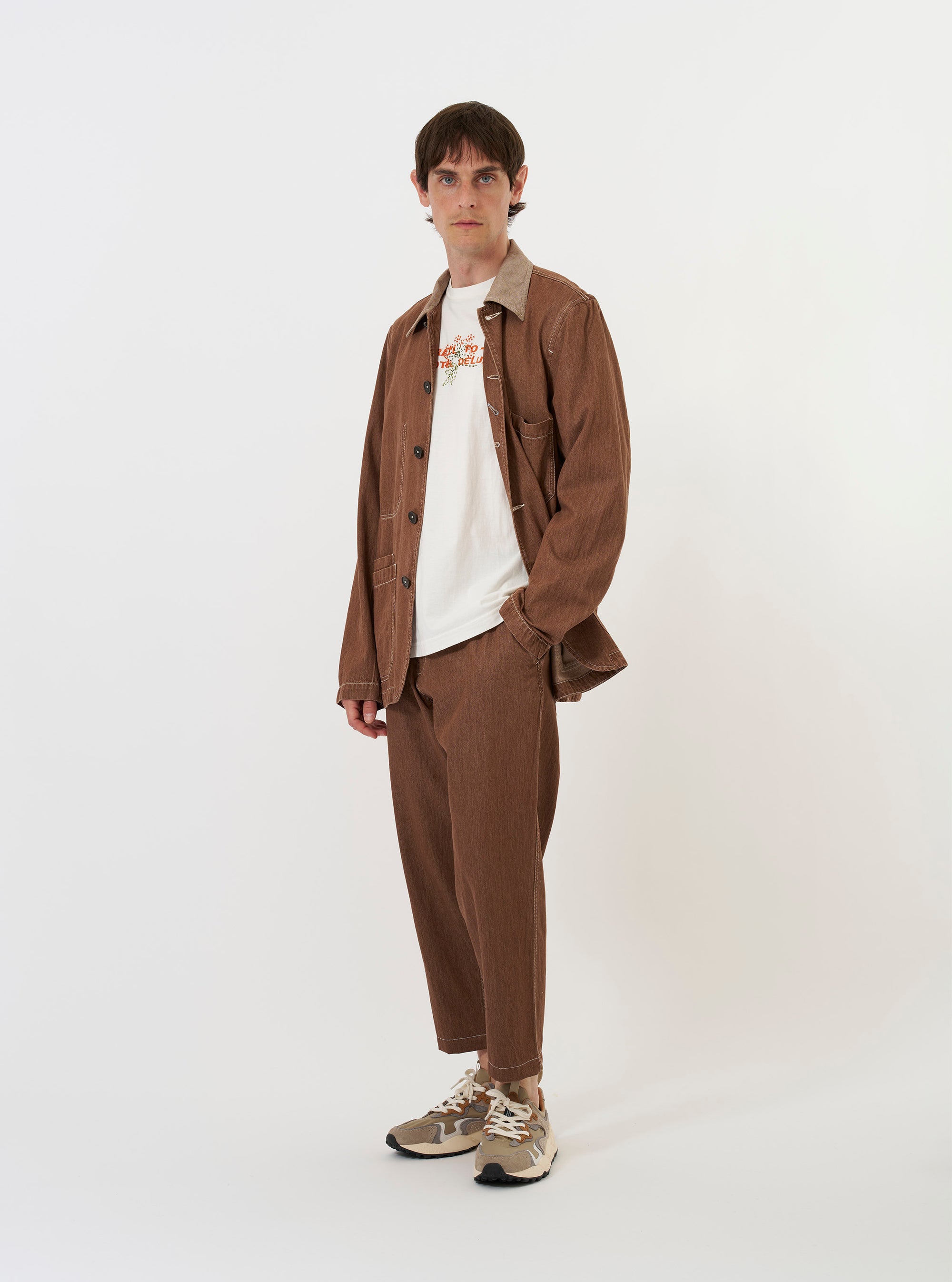 The Brown Meco Denim OG Bakers Jacket is shown laid flat against a plain white background. The jacket features a classic collar, a four-button front closure with a visible contrast top buttonhole, and a series of large patch pockets with angled corners. One chest pocket and two larger lower pockets are prominent, all highlighting the textured brown denim fabric and tonal stitching.