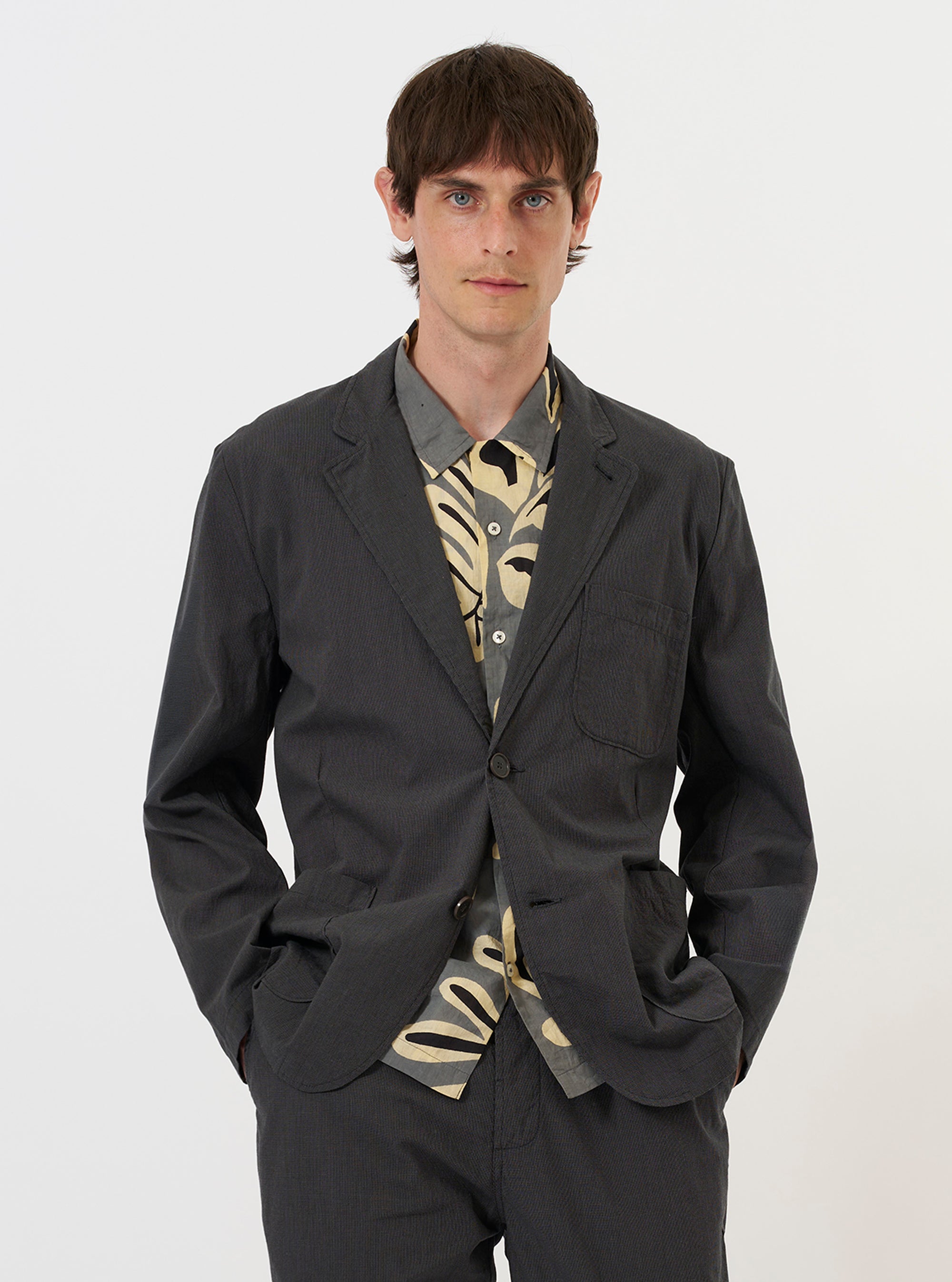 A model is wearing the Charcoal Seattle Cotton Two Button Jacket against a plain white background. The charcoal grey jacket features a classic two-button front closure, notched lapels, and a structured fit.