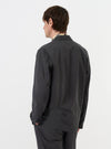 A model is seen from the back wearing the Charcoal Seattle Cotton Two Button Jacket against a plain white background. The image highlights the jacket's relaxed fit, structured shoulders, and central vent at the hem. The charcoal grey cotton fabric features a subtle basket-weave texture.