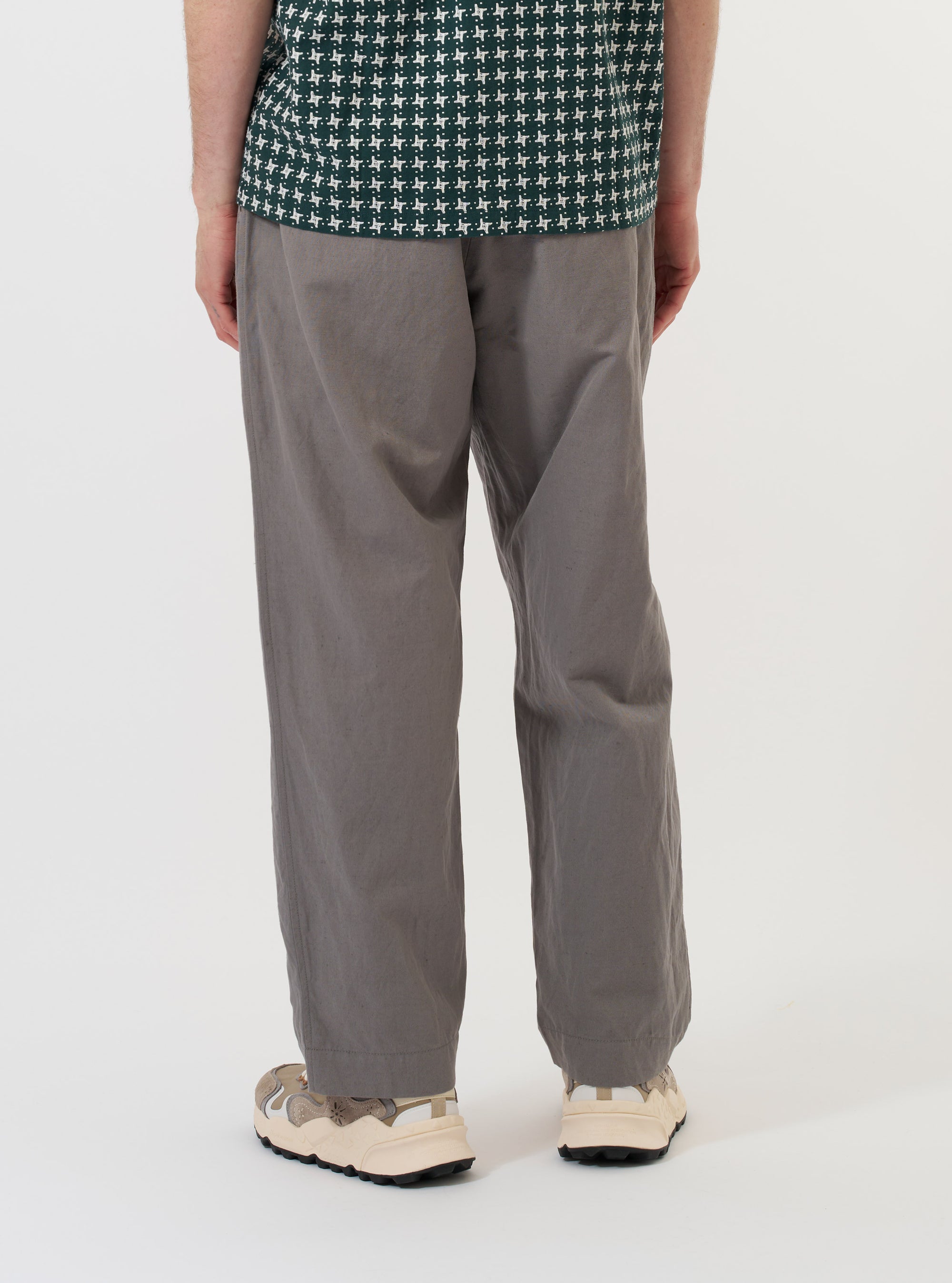 A model is wearing the Mid Grey Linen Slub Weave Oxford Pant against a plain white background. The image, captured from the rear, highlights the loose, wide-leg fit of the grey trousers, showing the elasticated waistband and one of the back pockets. No other garments are visible.