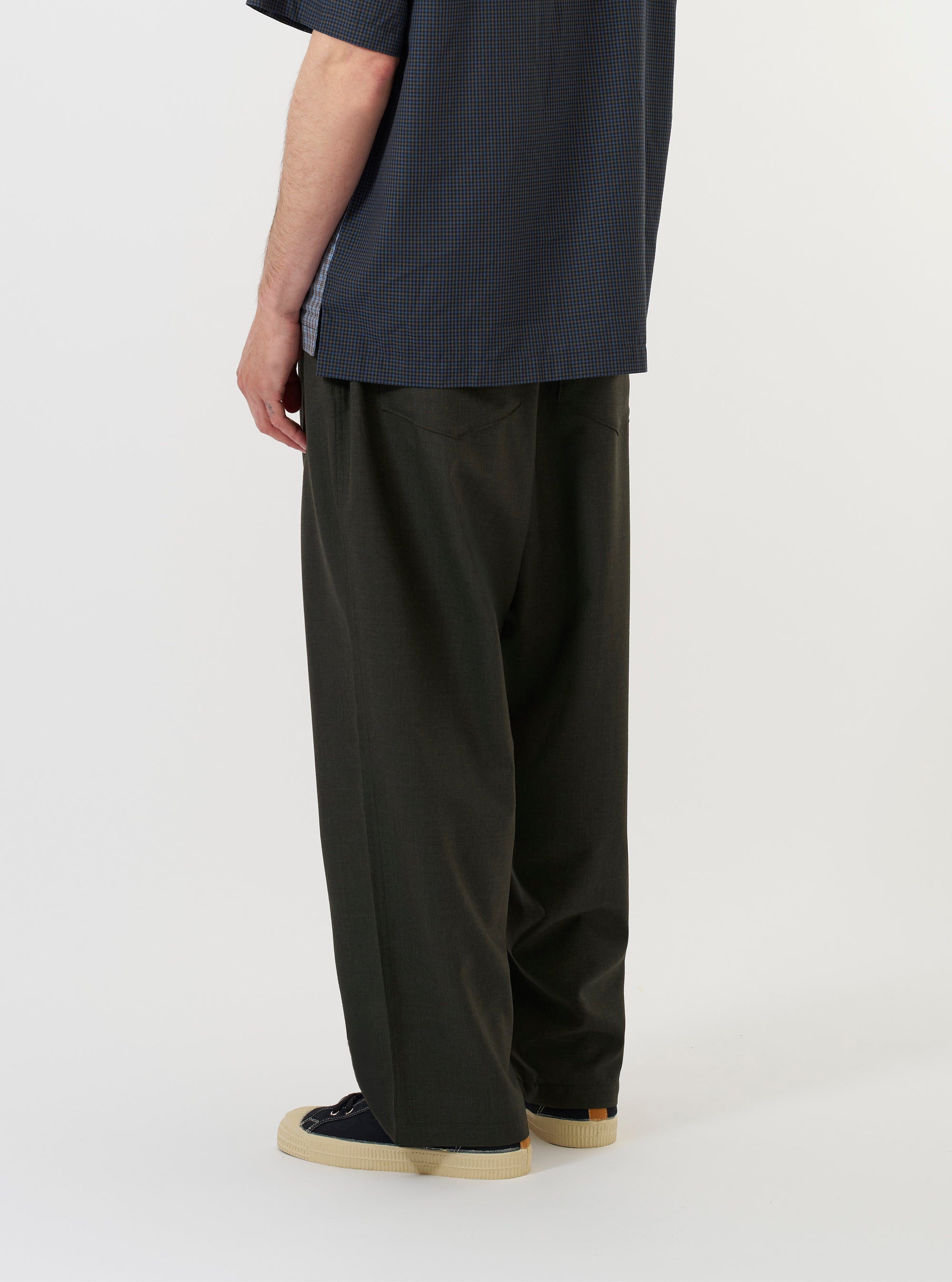A model is wearing the Olive Marl Tropical Suiting Dutch Pant against a plain white background. The image, captured from a side-rear perspective, highlights the wide-leg silhouette of the olive green trousers and features a visible side buckle waist adjuster.