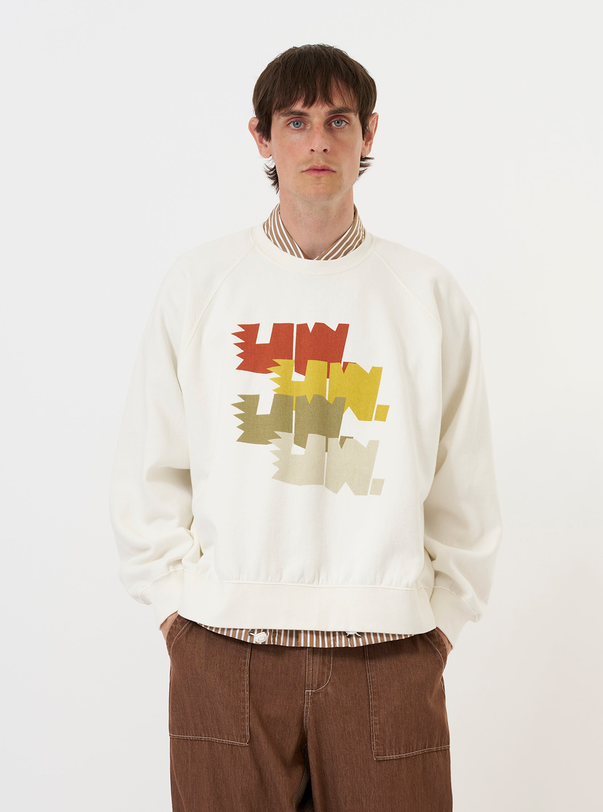 A model is wearing the Ecru Brush Back Sweat FM Raglan Sweatshirt against a plain white background. The image shows the sweatshirt from the front, highlighting the ribbed crew neck, raglan sleeves, and the soft, textured ecru cotton fabric. The model's hands are placed in the side pockets, showcasing the relaxed fit of the garment.
