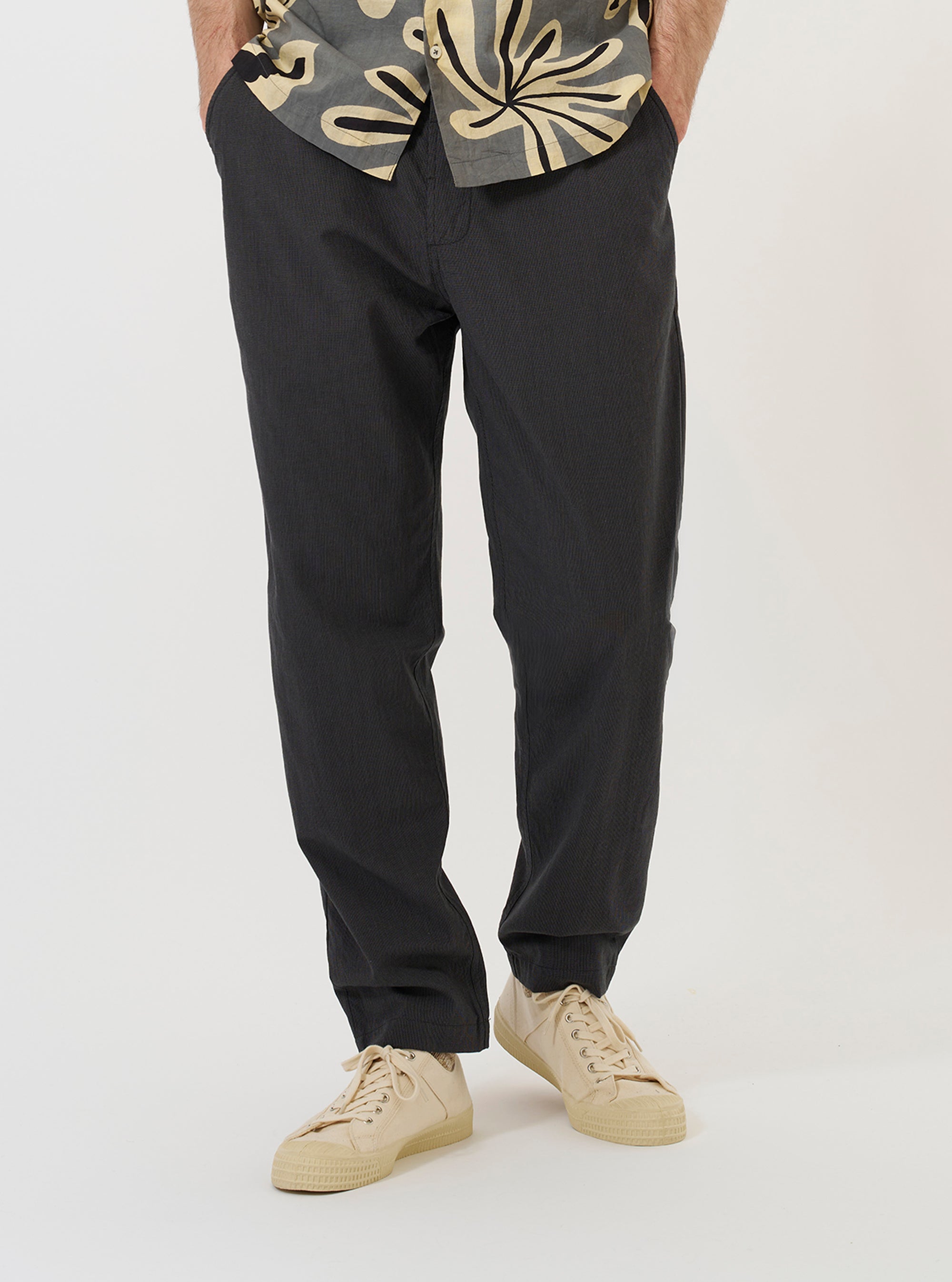 A model is wearing the Charcoal Seattle Cotton Military Chino against a plain white background. The charcoal grey trousers are shown from the waist down, featuring a straight leg fit, side slip pockets, and a visible buttoned waistband. The model is standing straight, pairing the chinos with dark-colored shoes.