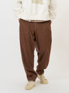 A model wears a pair of Brown Meco Denim Patched Fatigue Pants while standing against a plain white background. The trousers feature a straight-leg fit, large rectangular patch pockets on the front of the thighs, and a visible button fly. The model is also wearing a light-colored shirt and navy blue shoes.