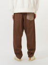 A model is wearing a pair of Brown Meco Denim Patched Fatigue Pants against a plain white background. The image provides a close-up view from the waist down, showcasing the straight-leg fit, large fatigue-style front patch pockets, and the texture of the brown denim. The model is standing and is also wearing navy blue footwear.