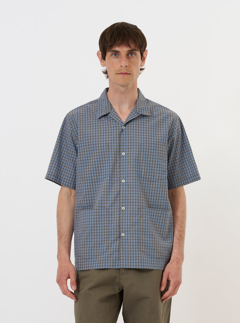 A pale blue check plaid summer overshirt is displayed flat against a plain white background. The garment features a standard pointed collar, a full button-down front, and two prominent utility chest pockets with buttoned flaps. The fabric has a light blue and white plaid pattern.