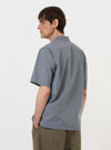 A model is seen from the back wearing the Pale Blue Check Plaid Summer Overshirt against a plain white background. The overshirt features a light blue and white plaid pattern, a straight hem, and a simple collar. The model is also wearing dark trousers.