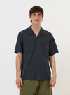 A model is wearing a Navy Check Plaid Summer Overshirt against a plain white background. The overshirt features a dark navy and white plaid pattern, a classic collar, and a full button-down front. The model is shown from the torso up, wearing the garment over a white t-shirt. The texture of the cotton-polyester fabric and the clean stitching of the collar and placket are prominent. No mannequin is present in the image.