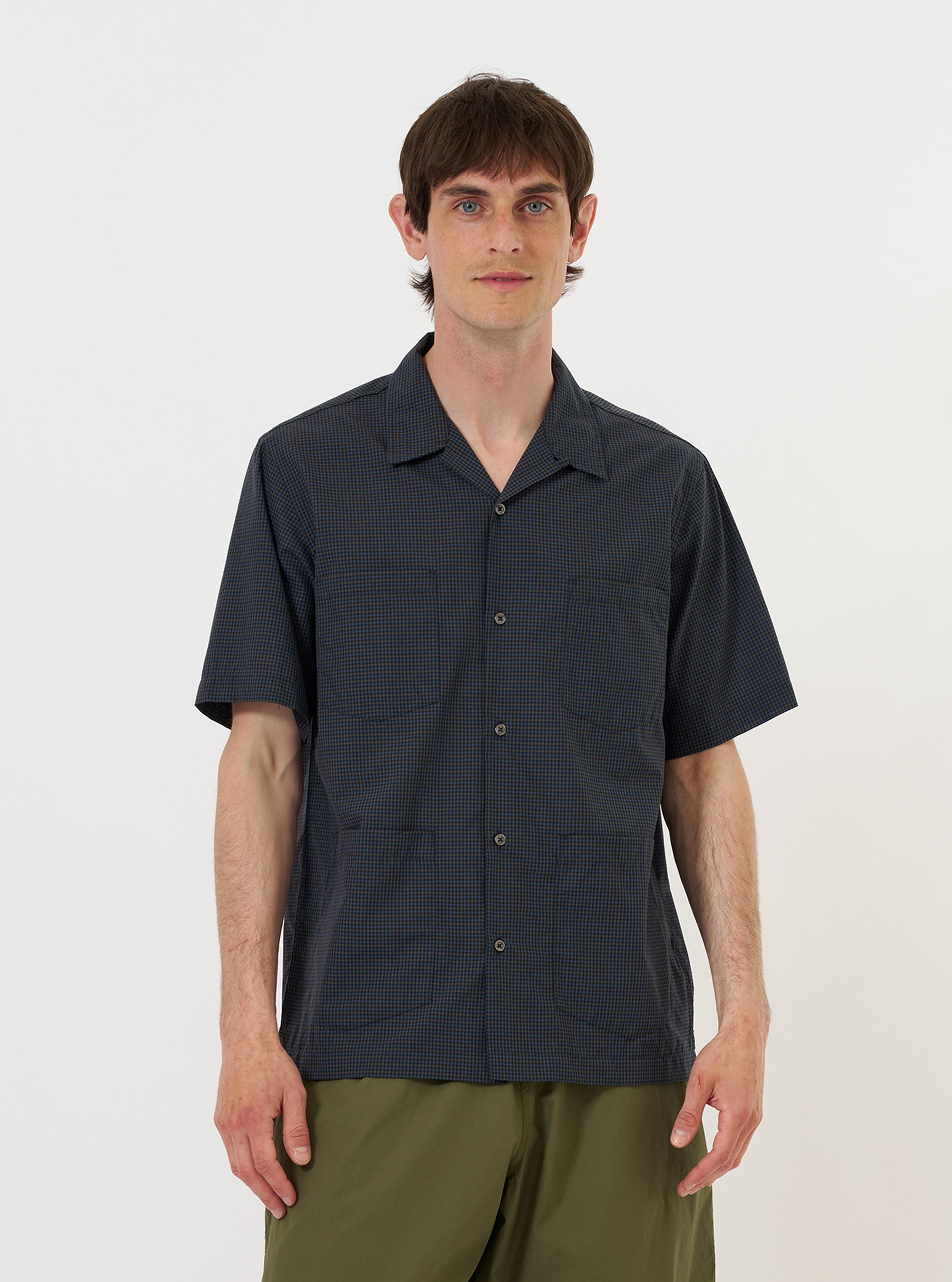 A model is wearing a Navy Check Plaid Summer Overshirt against a plain white background. The overshirt features a dark navy and white plaid pattern, a classic collar, and a full button-down front. The model is shown from the torso up, wearing the garment over a white t-shirt. The texture of the cotton-polyester fabric and the clean stitching of the collar and placket are prominent. No mannequin is present in the image.