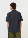A model is wearing the Navy Check Plaid Summer Overshirt against a plain white background. The image, taken from a side-rear perspective, showcases the overshirt's dark navy and white plaid pattern and relaxed fit. The model is standing with their hands by their sides, highlighting the length of the sleeves and the garment's drape.