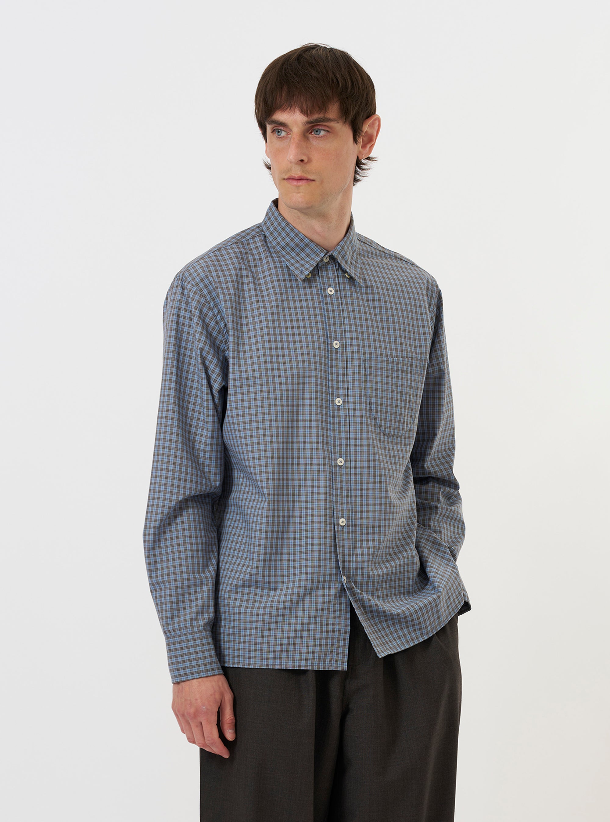 A model is wearing the Pale Blue Check Plaid Lazy Day Shirt against a plain white background. The shirt features a pale blue and white plaid pattern, a button-down front, and a classic collar. The model is wearing the shirt tucked out, paired with dark trousers. The focus is on the upper half of the garment and the fit on the model.