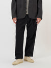A model is wearing the Black Broadcloth Oxford Pant against a plain white background. The trousers feature a loose, wide-leg fit with a pleated front and a drawstring visible at the waistband. The image captures the model from the waist down, highlighting the drape and texture of the black fabric.