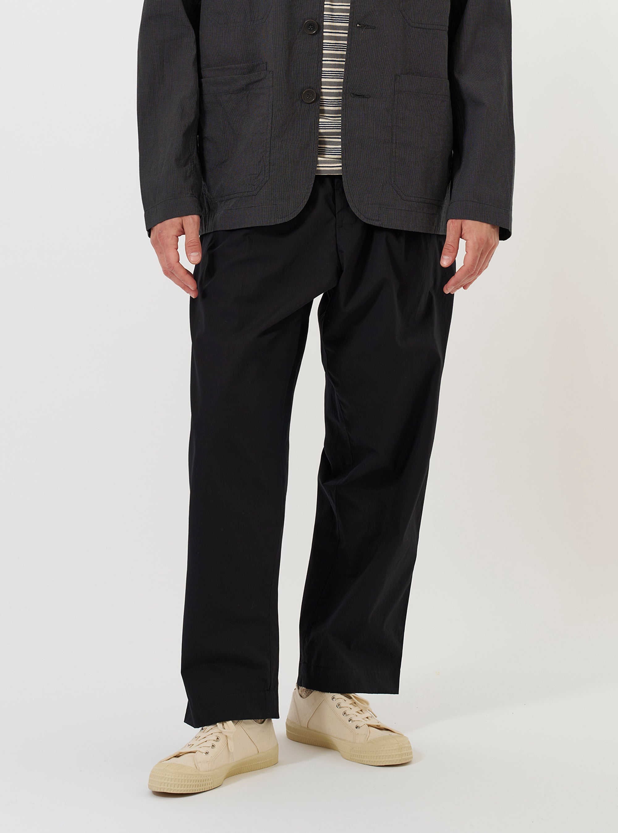 A model is wearing the Black Broadcloth Oxford Pant against a plain white background. The trousers feature a loose, wide-leg fit with a pleated front and a drawstring visible at the waistband. The image captures the model from the waist down, highlighting the drape and texture of the black fabric.