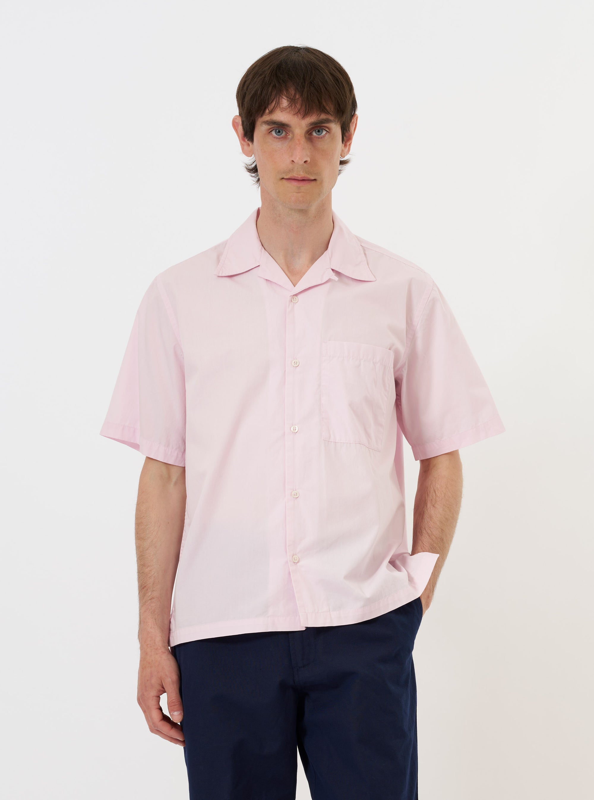 A Pale Pink Broadcloth Camp Shirt is shown laid flat against a solid white background. The garment features a relaxed camp collar, a full button-down front with tonal buttons, short sleeves, and a straight hem. The light pink cotton fabric has a smooth, matte finish.