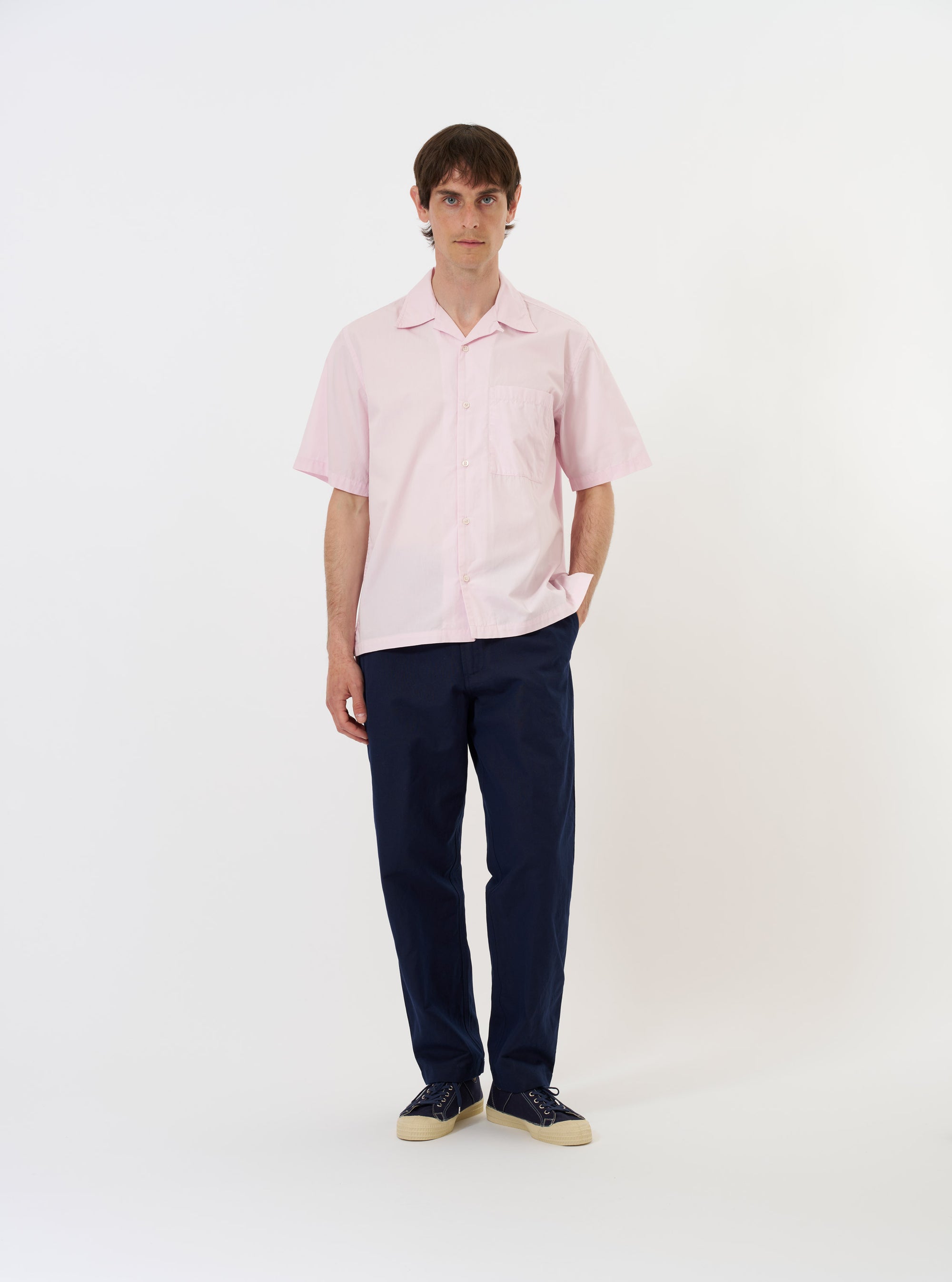 The Pale Pink Broadcloth Camp Shirt is shown laid flat against a solid white background. The shirt features a classic camp collar, a full button-down front, and a single patch pocket on the left chest. The short-sleeved garment is made from a smooth, light pink cotton broadcloth fabric.