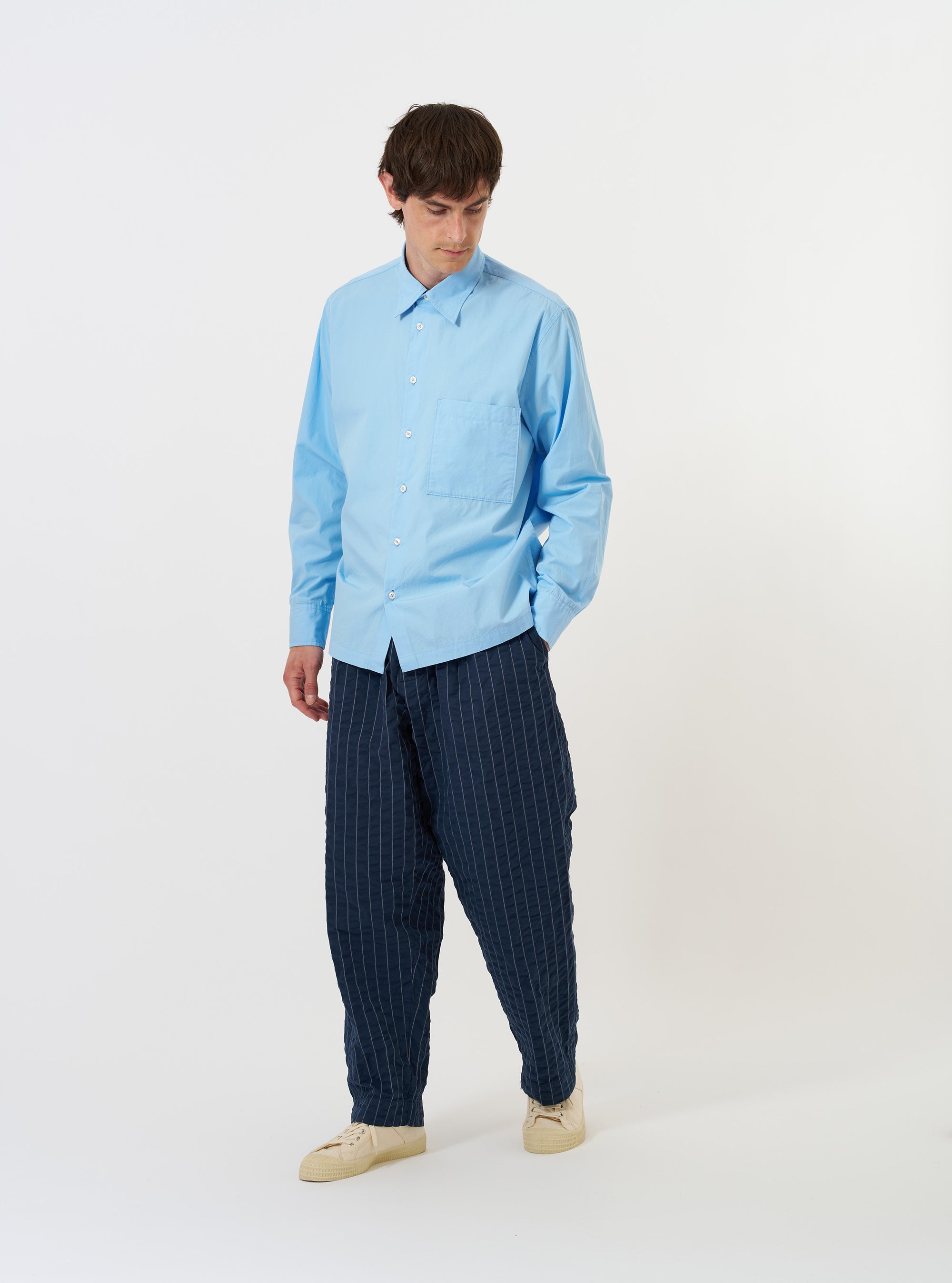 The Pale Blue Broadcloth Lucky Shirt is shown laid flat against a solid white background. The garment features a light blue color, a classic pointed collar, a full button-down front, and a single chest pocket on the left side. The long sleeves are spread to the sides, and the hem appears straight.