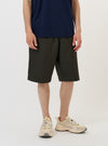 A model stands against a plain white background wearing the Olive Marl Tropical Suiting Vacation Short. The image highlights the relaxed, knee-length fit of the olive green shorts, featuring a visible drawstring at the elasticated waistband and side seam pockets. The garment is paired with a matching short-sleeve shirt and dark shoes.