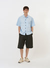 The Sky Blue Paper Touch Cotton S/S Fatigue Shirt is shown as a flat lay against a plain white background. The short-sleeved overshirt features a light blue color, a standard pointed collar, a full button-down front, and a single large patch pocket on the left chest.