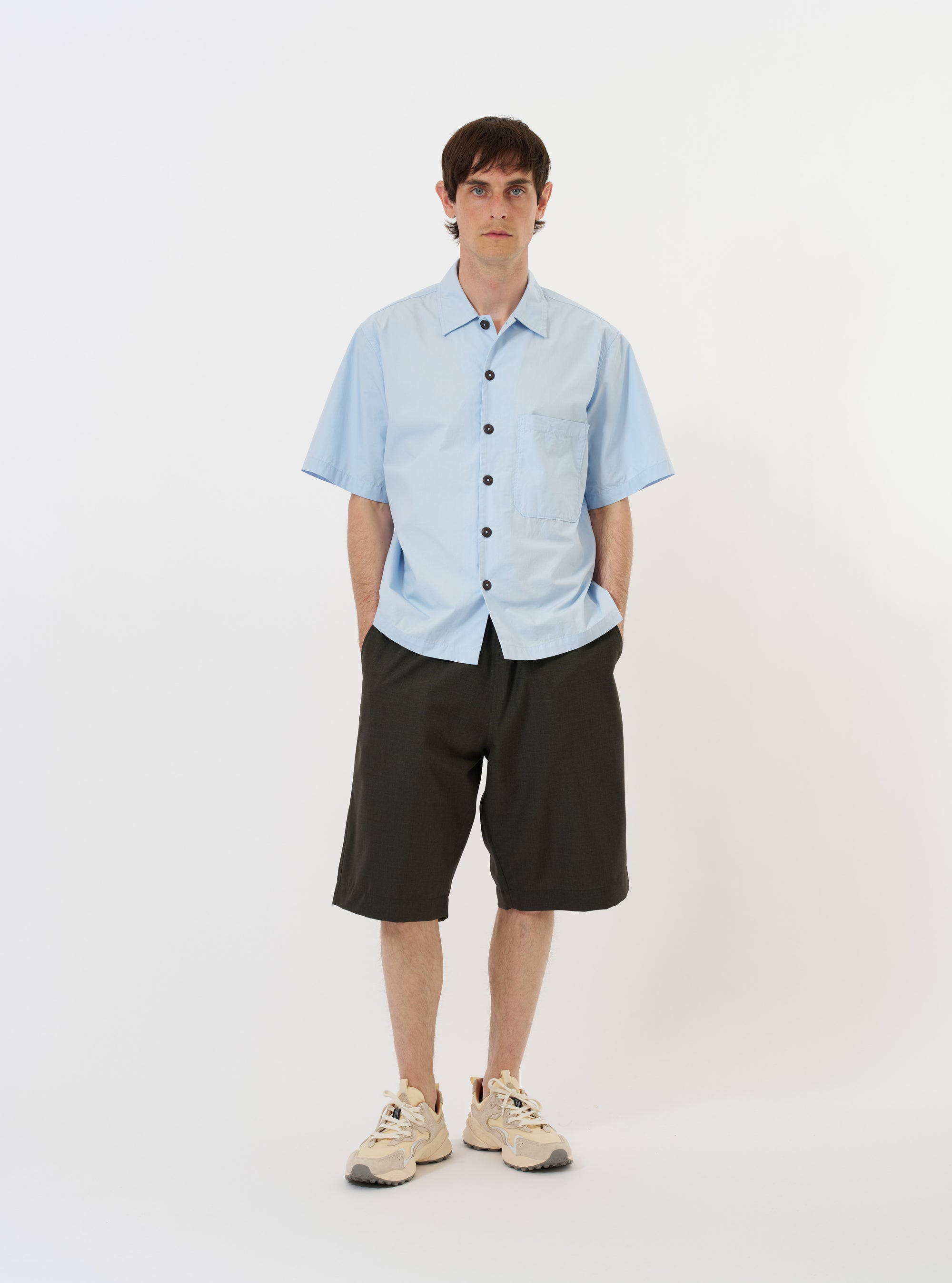 The Sky Blue Paper Touch Cotton S/S Fatigue Shirt is shown as a flat lay against a plain white background. The short-sleeved overshirt features a light blue color, a standard pointed collar, a full button-down front, and a single large patch pocket on the left chest.