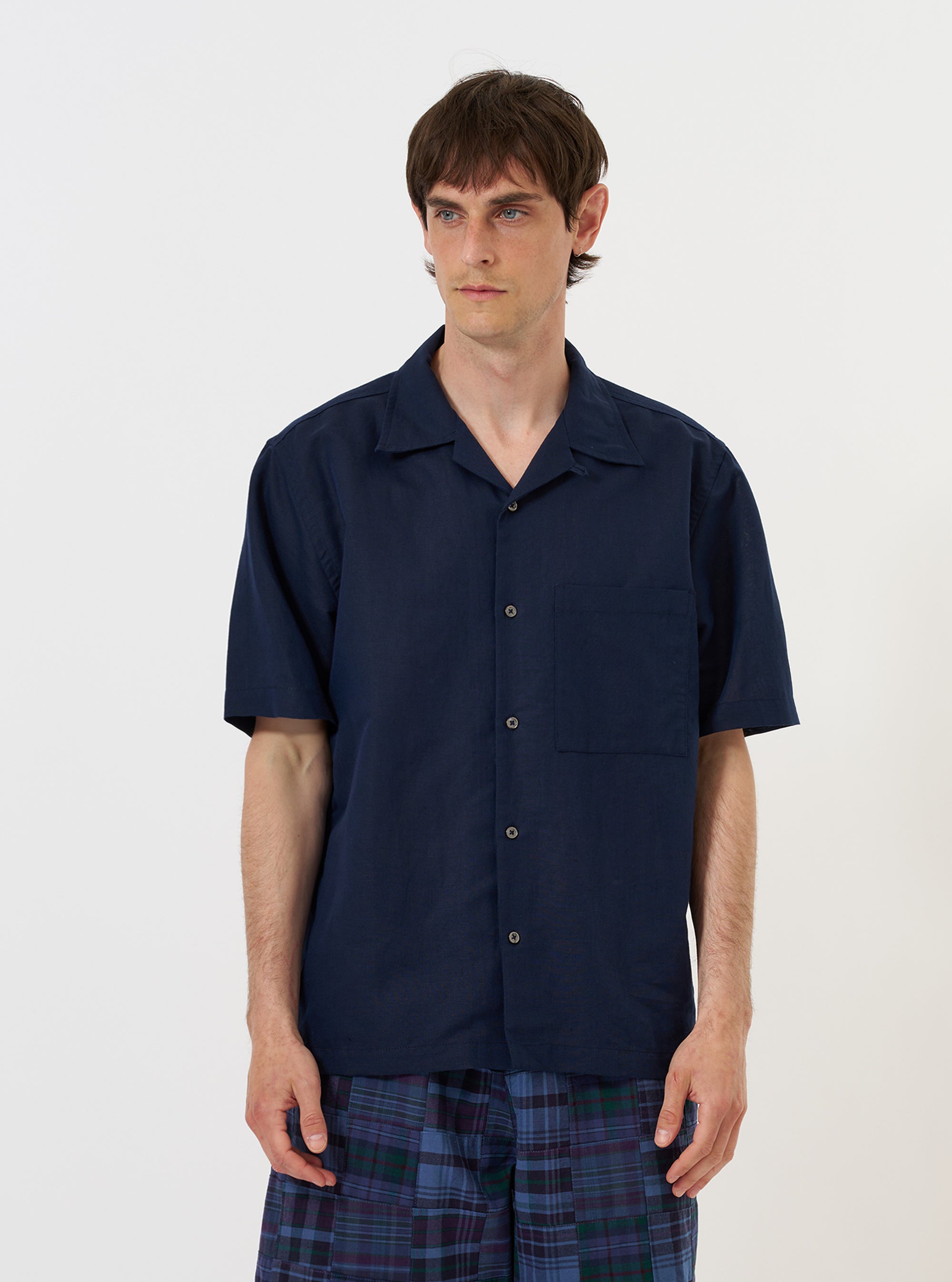 A model is wearing the Navy Linen Cotton Shirting Camp Shirt against a plain white background. The shirt features a relaxed fit with a camp collar, short sleeves, and a full button-down front. The model is standing straight, and the image captures the garment from the waist up, highlighting the texture of the navy linen-cotton blend.