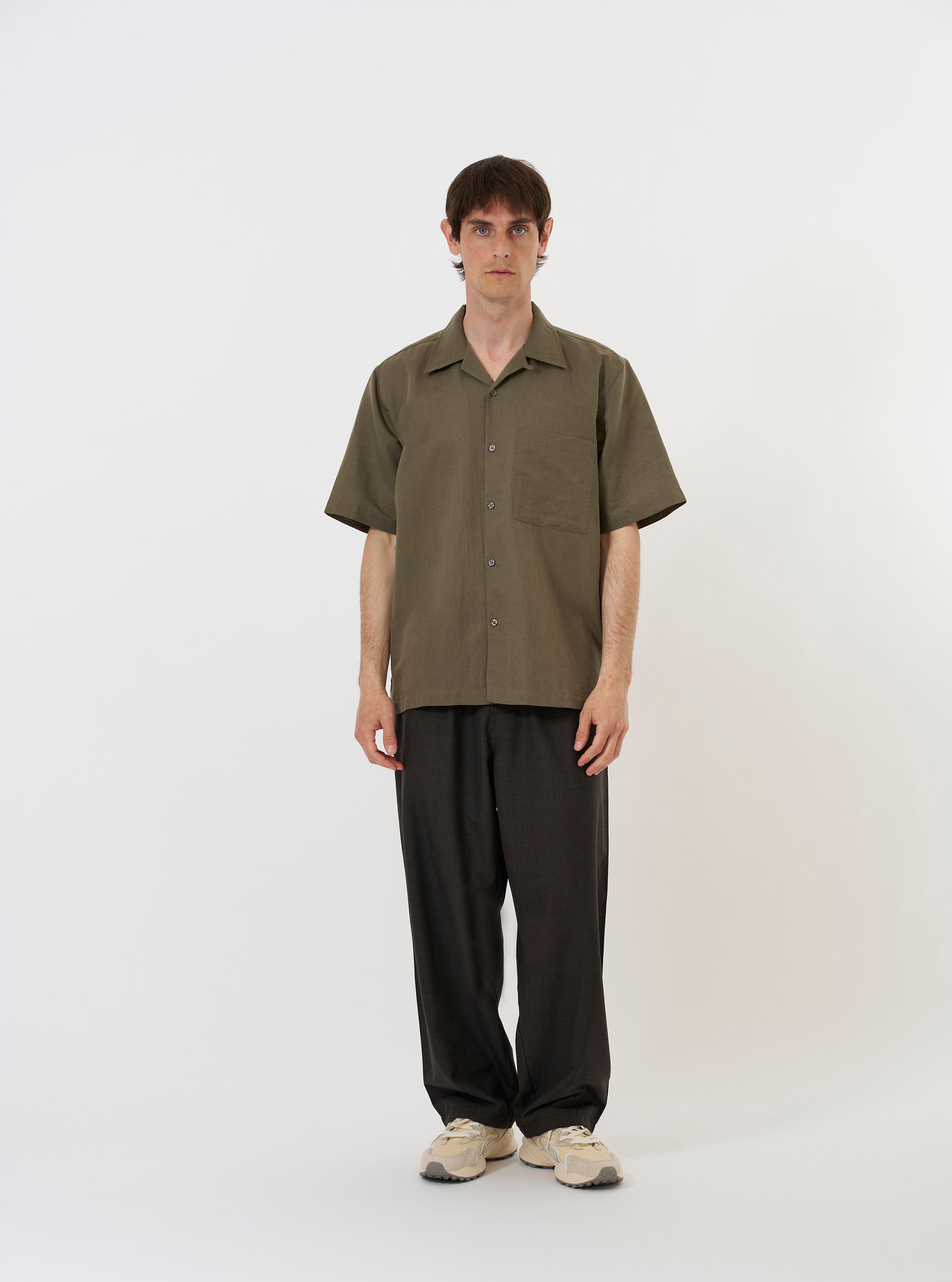 The Olive Linen Cotton Shirting Camp Shirt is shown laid flat against a solid white background. The shirt features a camp collar, a button-down front with tonal buttons, and a single chest pocket on the left side. The garment has short sleeves and a straight hem, with the olive green fabric showing a subtle linen texture.