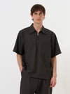 A male model is wearing the Brown Marl Tropical Suiting Ewan Shirt against a plain white background. The short-sleeved, pullover shirt features a 1/4 zip neck, which is worn open, and a classic pointed collar. The garment has a relaxed, wide fit and is made from a textured brown marl fabric. The model is shown from the waist up, pairing the shirt with a light-colored undershirt. No mannequin is present in the image.