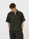 A model is wearing the Olive Marl Tropical Suiting Ewan Shirt against a plain white background. The short-sleeved shirt is shown from the front with the quarter-zip neckline partially open, highlighting its relaxed fit and olive green marl fabric.
