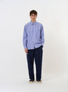 The Blue/White Cotton Stripe Square Pocket Shirt is shown laid flat against a solid white background. The garment features a light blue and white vertical stripe pattern, a classic pointed collar, and a full button-down front. A prominent, oversized square patch pocket is positioned on the left chest. The shirt has long sleeves with buttoned cuffs and a slightly curved hem.