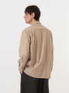 A model is wearing the Brown/White Cotton Stripe Square Pocket Shirt against a plain white background. The image shows the shirt from the back, highlighting the clean back yoke, long sleeves, and the fine brown and white vertical stripe pattern of the cotton fabric. The model is wearing the shirt untucked, paired with dark trousers.