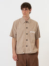 A model is wearing the Brown/White Cotton Stripe Z Tech Overshirt against a plain white background. The overshirt features a brown and white vertical stripe pattern, a classic pointed collar, and a full button-down front. A prominent zipped patch pocket is visible on the chest. The model is shown from the chest up, wearing the garment over a white t-shirt.