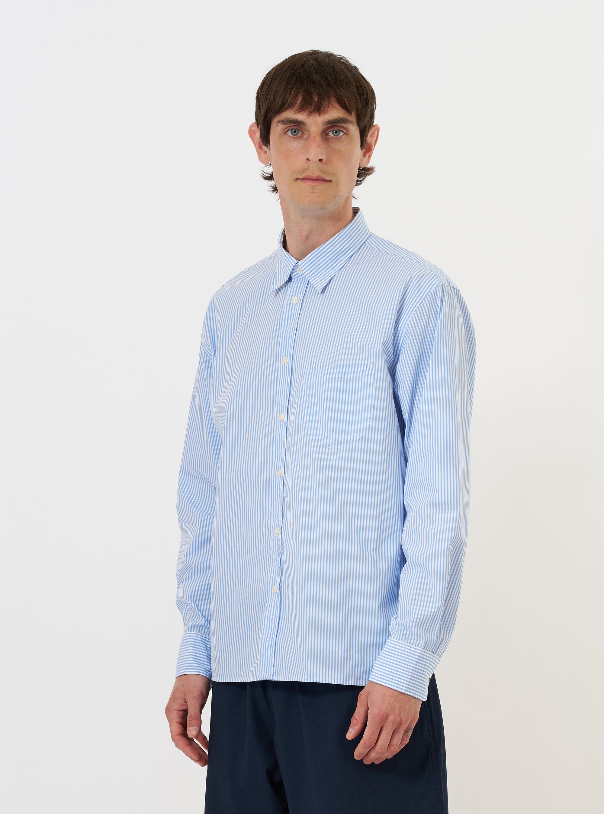A model is wearing the Sky/White Classic Nipon Stripe Lazy Day Shirt against a plain white background. The shirt features a light blue and white vertical stripe pattern, a classic pointed collar, and a full button-down front. The model is shown from the torso up, wearing the garment over a white t-shirt.