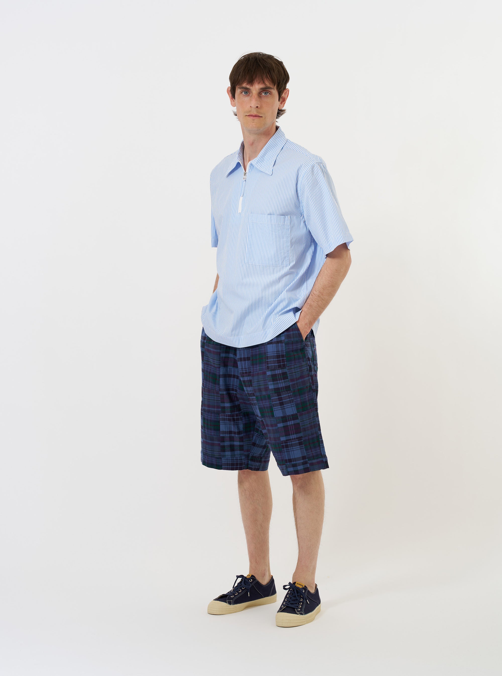 The Sky/White Classic Nipon Stripe Ewan Shirt is shown laid flat against a solid white background. The garment features a light blue and white vertical stripe pattern, a half-zip front opening, a classic pointed collar, and a single chest pocket on the left side. The short sleeves and straight hem are clearly visible.