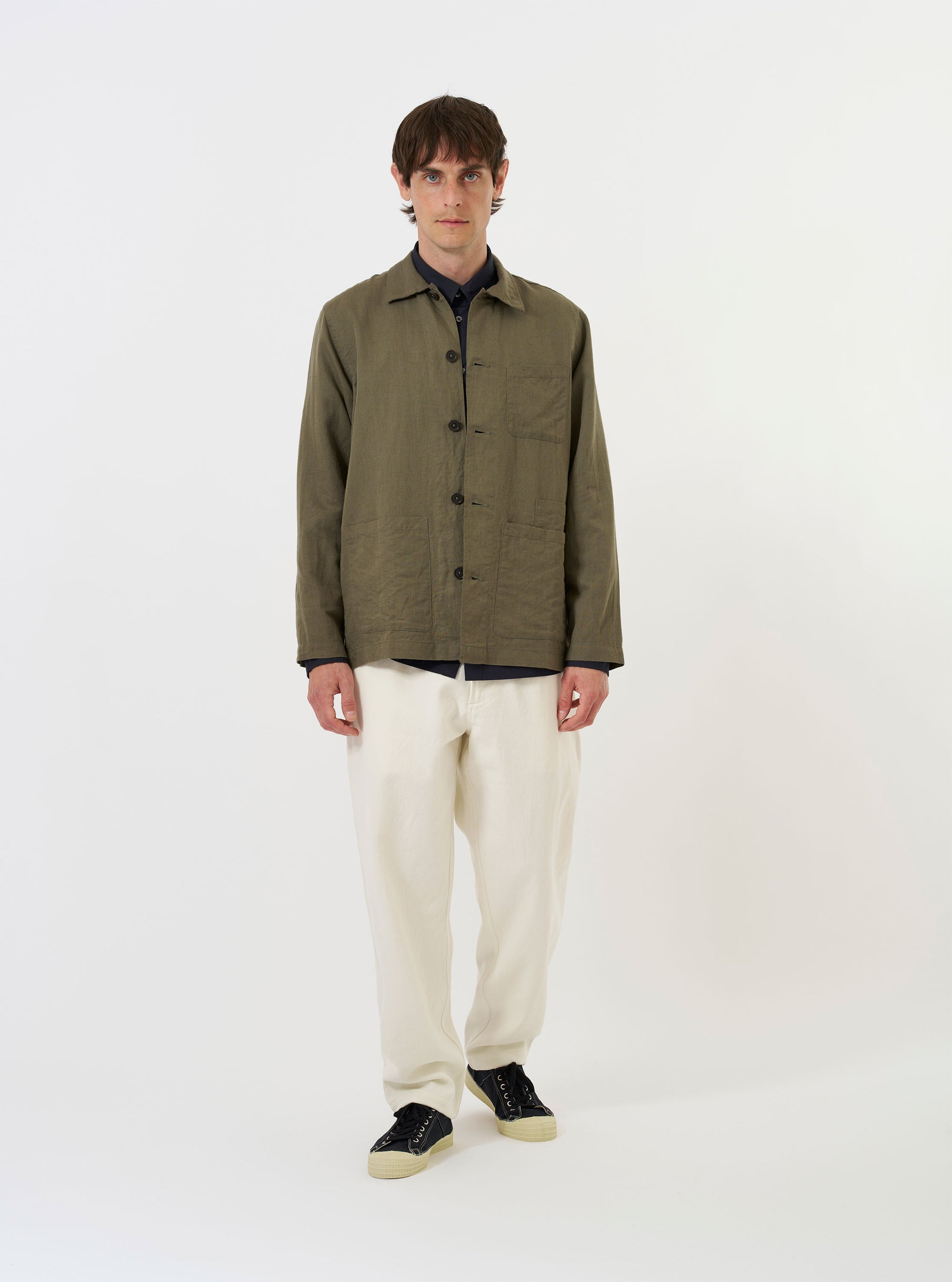The Olive Linen Cotton Shirting Bakers Overshirt is displayed laid flat against a solid white background. The garment features a classic one-piece collar, a full button-down front, and four front patch pockets: one asymmetric chest pocket, two large lower pockets, and a smaller partially concealed coin pocket. The overshirt is shown in an olive green color with a straight hem and plain cuffs.
