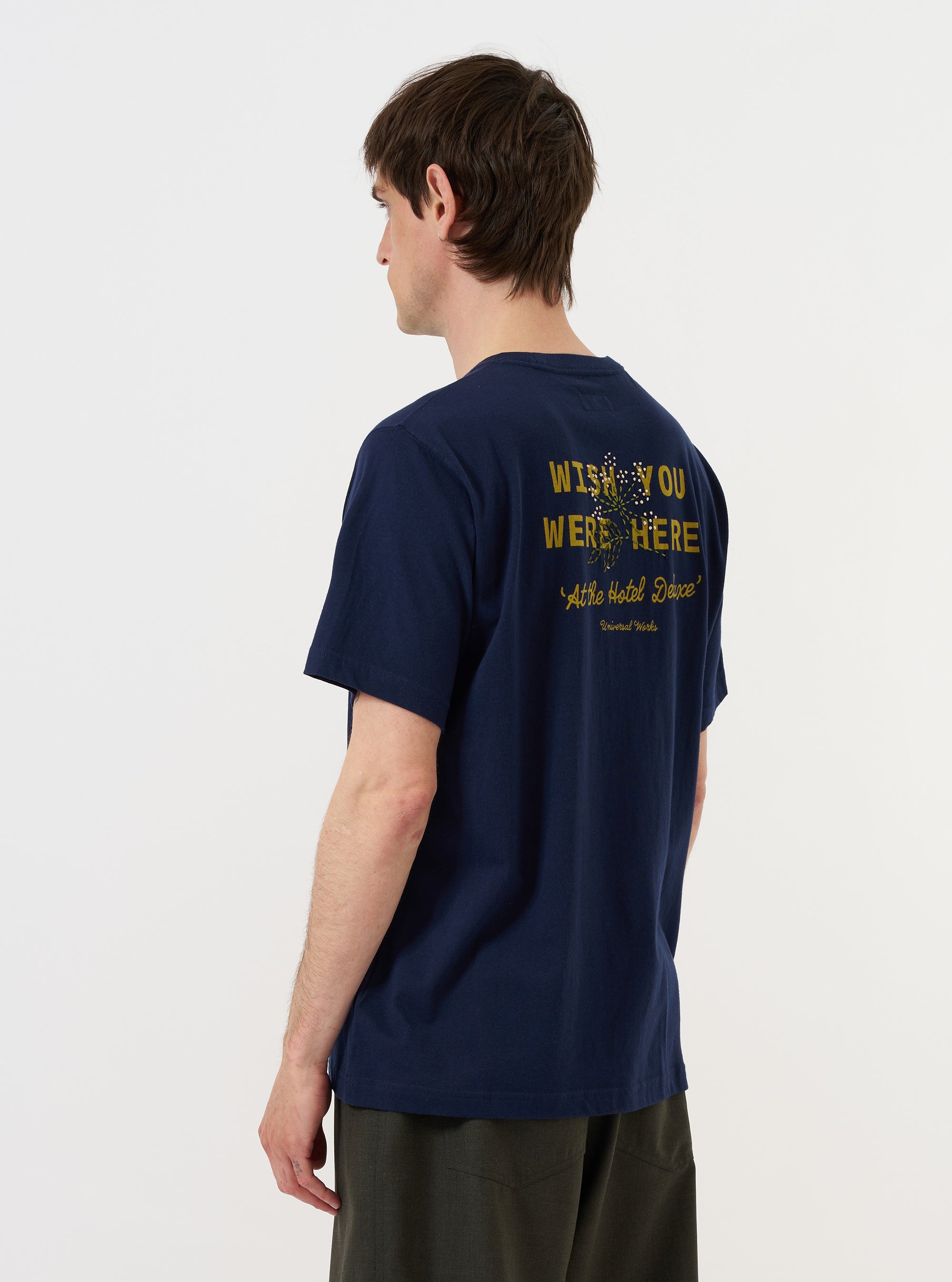 A model is shown from the back wearing the Navy Single Jersey Wish Wish You Were Here Tee against a plain white background. The navy blue t-shirt features a relaxed fit, short sleeves, and a prominent white graphic print on the back that reads "Wish You Were Here" in a stylized font.
