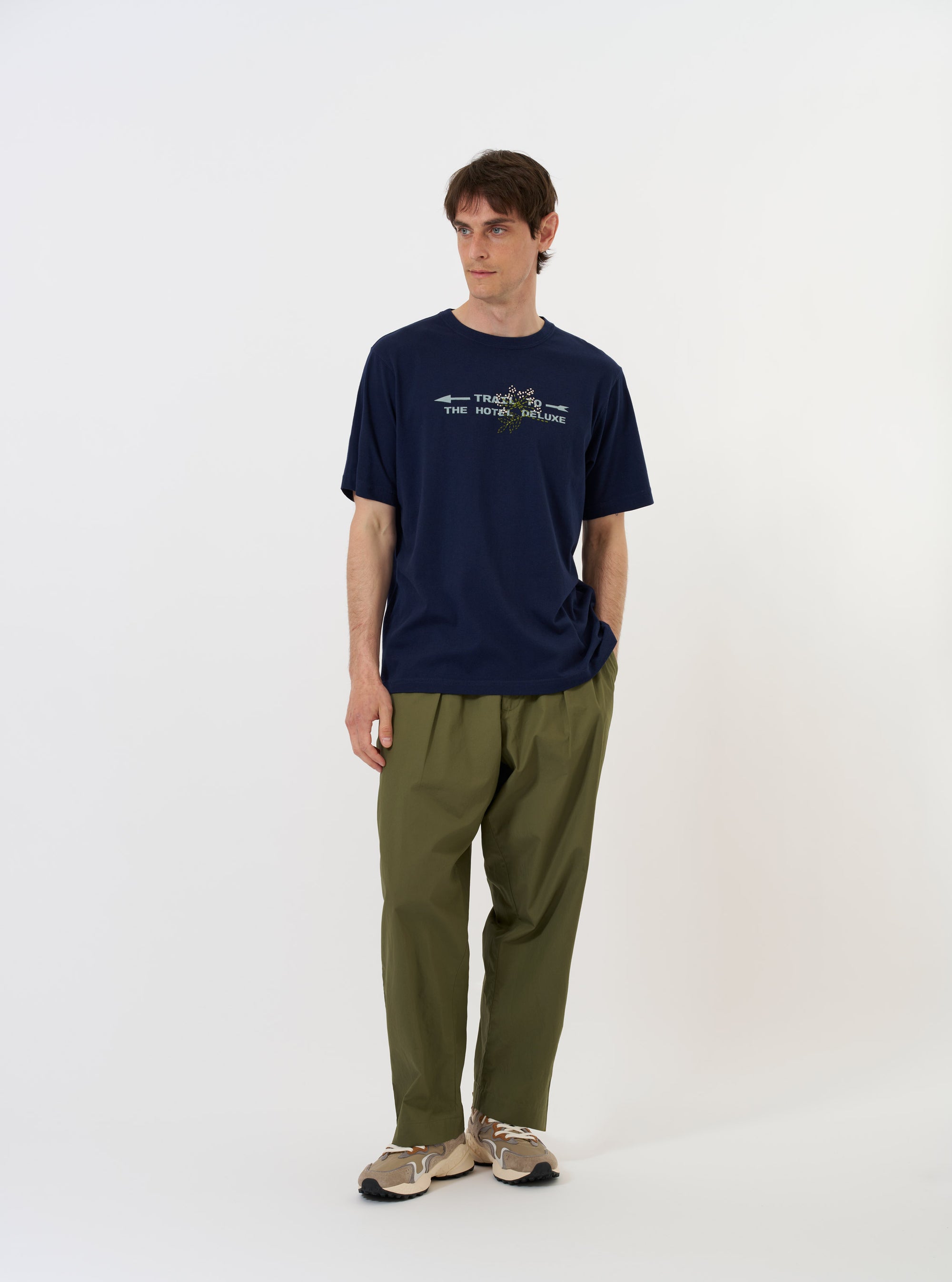 The Navy Single Jersey Trail Trail To Hotel Delux Tee is shown laid flat against a solid white background. The navy blue short-sleeved t-shirt features a classic crew neckline and a prominent white graphic print on the chest that reads Trail Trail to Hotel Delux.