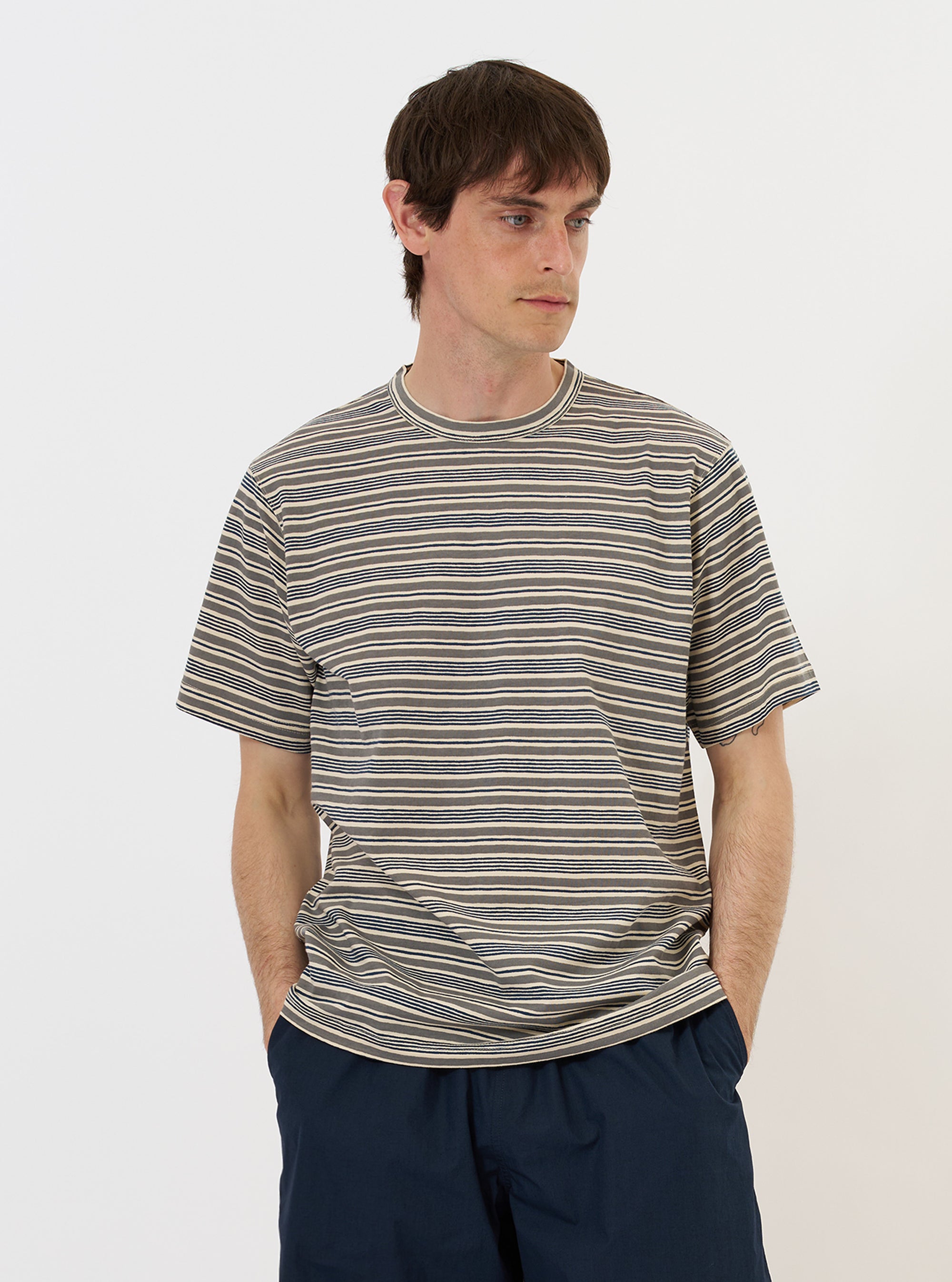 A model is wearing the Grey OS Stripe Jersey Core Tee against a plain white background. The short-sleeved t-shirt features horizontal grey and white stripes with a soft, irregular hand-painted character and a ribbed crew neck. The image shows the model from the chest up, highlighting the generous fit and the texture of the cotton jersey fabric.