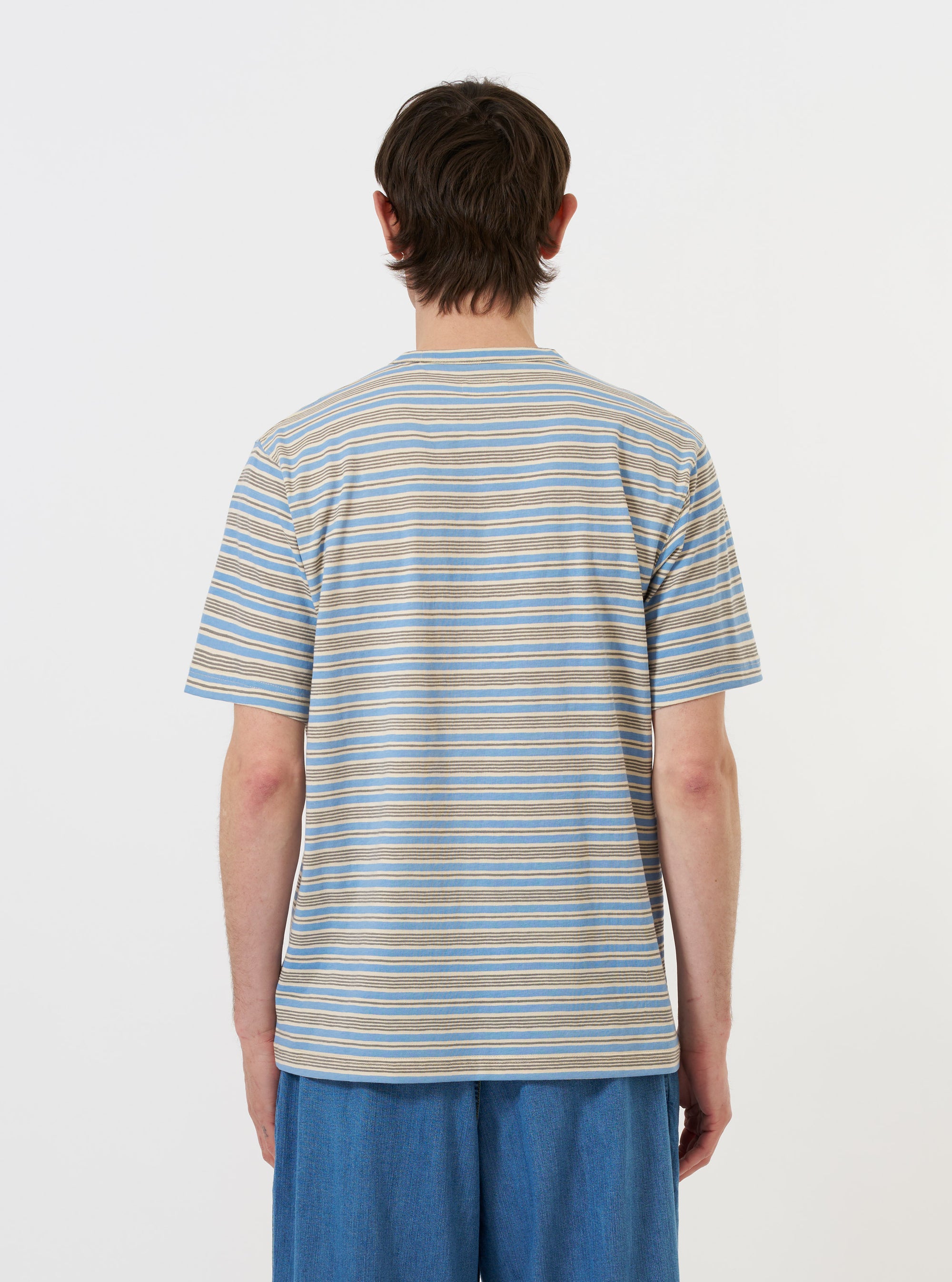 The Pale Blue OS Stripe Jersey Core Tee is shown from the back, laid flat against a plain white background. The image highlights the horizontal light blue and white stripes, the short sleeves, and the clean, straight hem of the garment.
