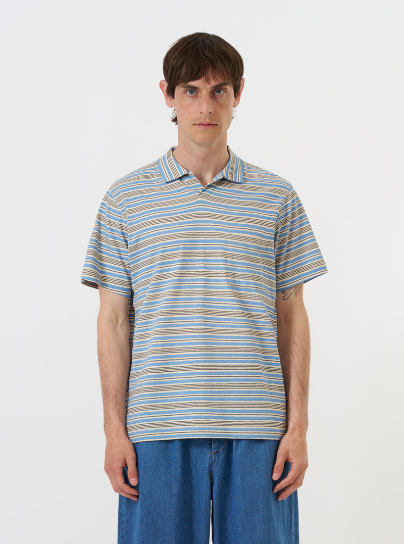 The Pale Blue OS Stripe Jersey Vacation Polo is shown laid flat against a plain white background. The shirt features a light blue and white horizontal stripe pattern, a relaxed open neck with a single-piece collar, a short front placket, and a single patch pocket on the left chest.