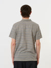 A model stands against a plain white background wearing the Grey OS Stripe Jersey Vacation Polo. The image shows the garment from the back, highlighting the grey and white horizontal stripes, the straight hem, and the relaxed fit of the short-sleeved polo shirt.