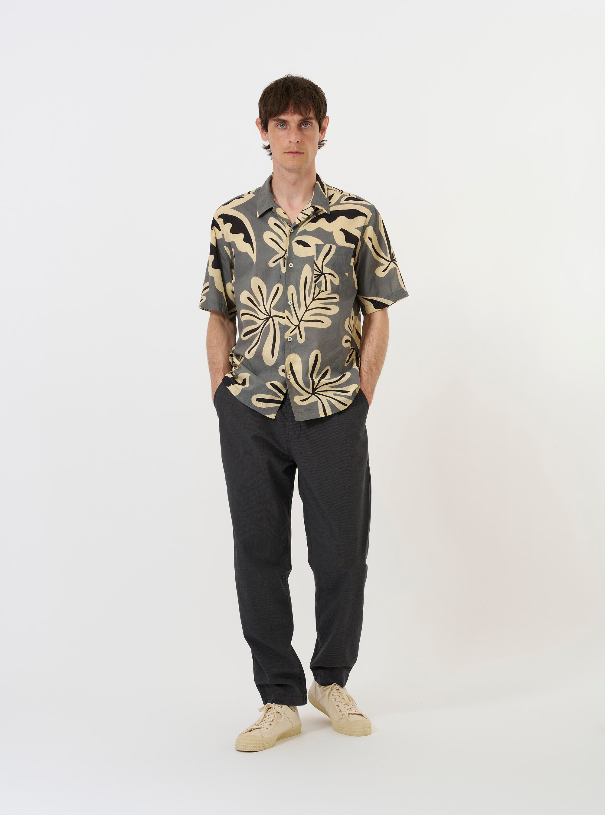 The Grey Baja Print Road Shirt is shown laid flat against a solid white background. This short-sleeve button-down features an all-over grey and white botanical print, a relaxed camp collar, and a single chest patch pocket on the left side. The garment has a straight hem and tonal buttons along the front.