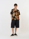 The Black Baja Print Road Shirt is shown laid flat against a solid white background. The shirt features a short-sleeve silhouette with a black and grey patterned Baja print throughout. Key details include a camp collar with a loop closure at the neck, a full button-down front, a single chest patch pocket, and a straight hem.