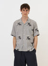 A model is wearing the Grey Hand Embroidered Stripe Cotton Road Shirt against a plain white background. The shirt features a grey and white vertical stripe pattern with intricate hand-embroidered details, a relaxed camp collar, and a button-down front. The model is shown from the chest up, highlighting the texture of the cotton fabric and the unique embroidery.
