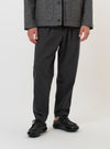 A model is wearing the Charcoal Seattle Cotton Pleated Track Pant against a plain white background. The charcoal grey trousers are shown from the waist down, featuring a loose, tapered fit with a single pleat at the waist and a drawstring waistband. The model is standing and has their hands in the side slip pockets.