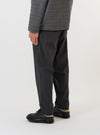 A model is wearing the Charcoal Seattle Cotton Pleated Track Pant against a plain white background. The charcoal grey trousers are shown from the waist down, highlighting the loose fit, tapered leg, and single pleat detail at the front. The elasticated waistband with a visible drawstring is also prominent as the model stands facing slightly to the side.
