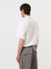 A model is seen from the back wearing the White Poplin Frill Shirt against a plain white background. The shirt features a clean white cotton poplin fabric with a prominent ruffled or frilled trim along the back yoke and shoulders. The model is also wearing dark trousers, and the image highlights the crisp texture and unique decorative detailing of the garment's rear construction. No mannequin is present in the image.