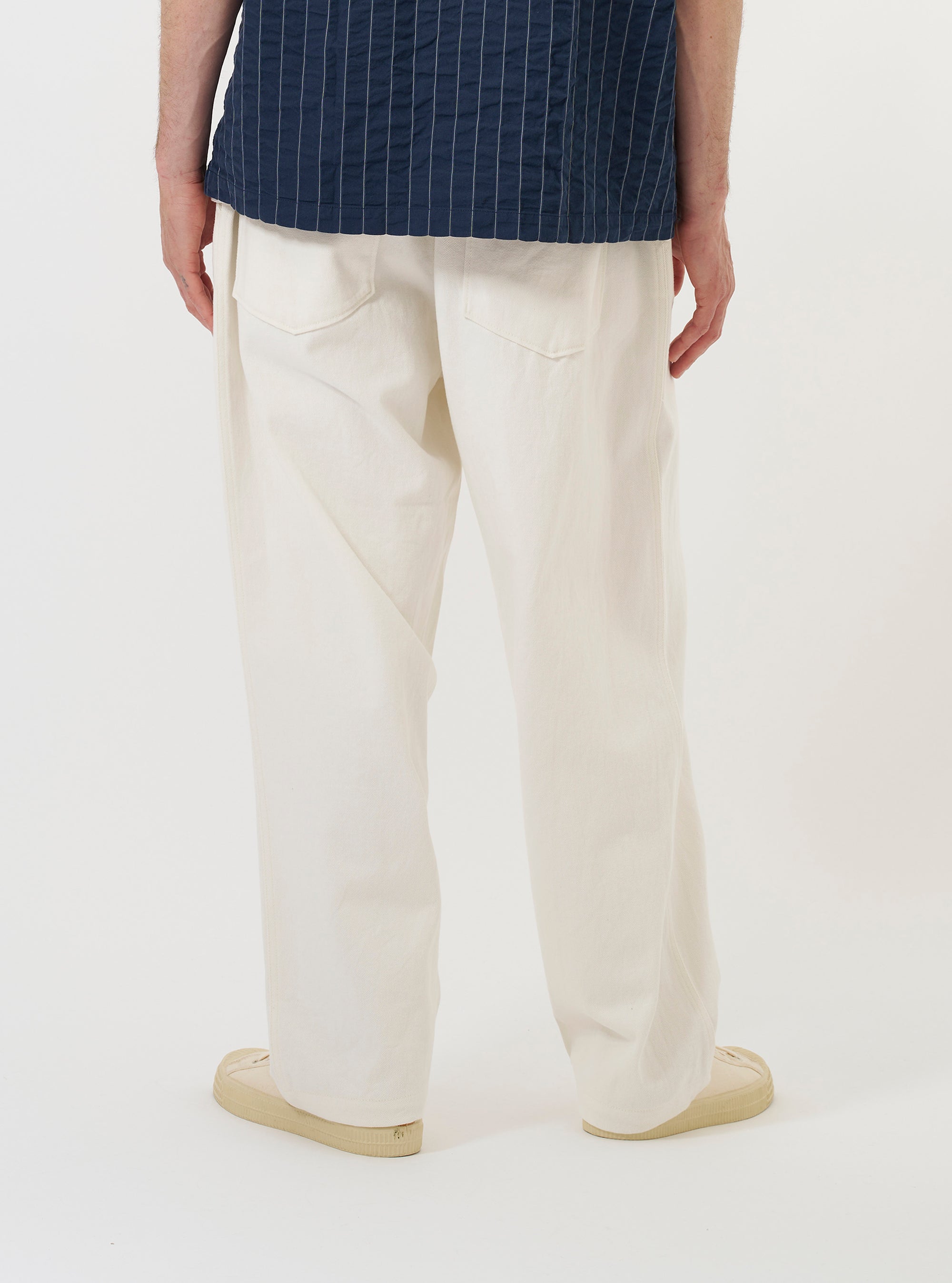 A model is wearing the Ecru Slub Drill Dutch Pant against a plain white background. The image provides a side-rear view of the trousers from the waist down, highlighting the loose, wide-leg fit and a single large patch pocket on the back. The model is also wearing navy blue shoes.