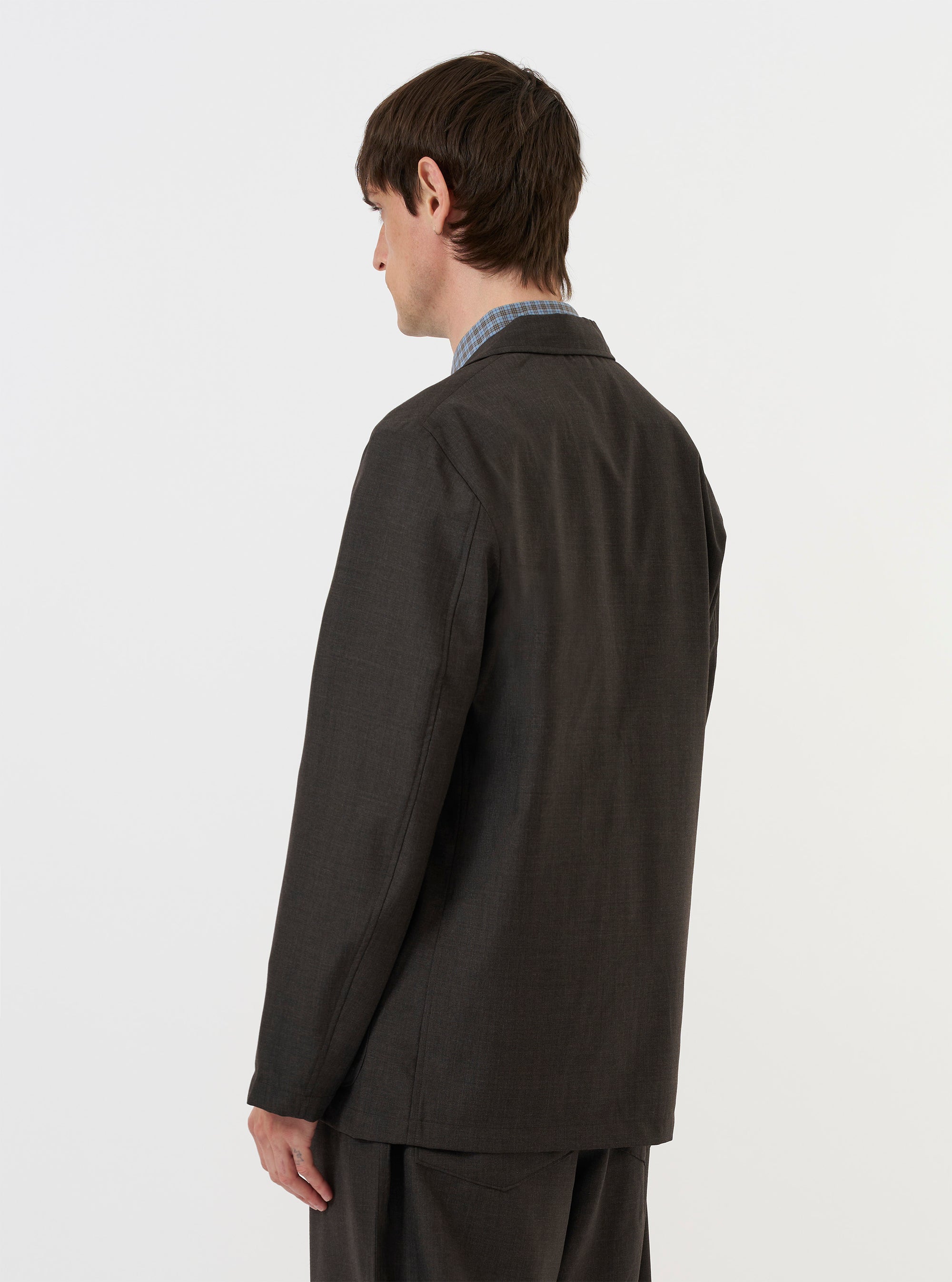 A model is wearing the Brown Marl Tropical Suiting Two Button Jacket against a plain white background. The image is taken from a rear-side perspective, showing the back of the jacket, its structured shoulders, and the fit of the sleeves. The brown marl fabric is prominent. No mannequin is present.