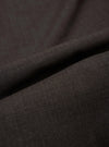 A close-up fabric swatch of the Brown Marl Tropical Suiting Pleated Track Pant shows a detailed view of the marled brown wool-blend material. The image highlights the fine, multi-tonal weave and smooth texture of the tropical suiting fabric.