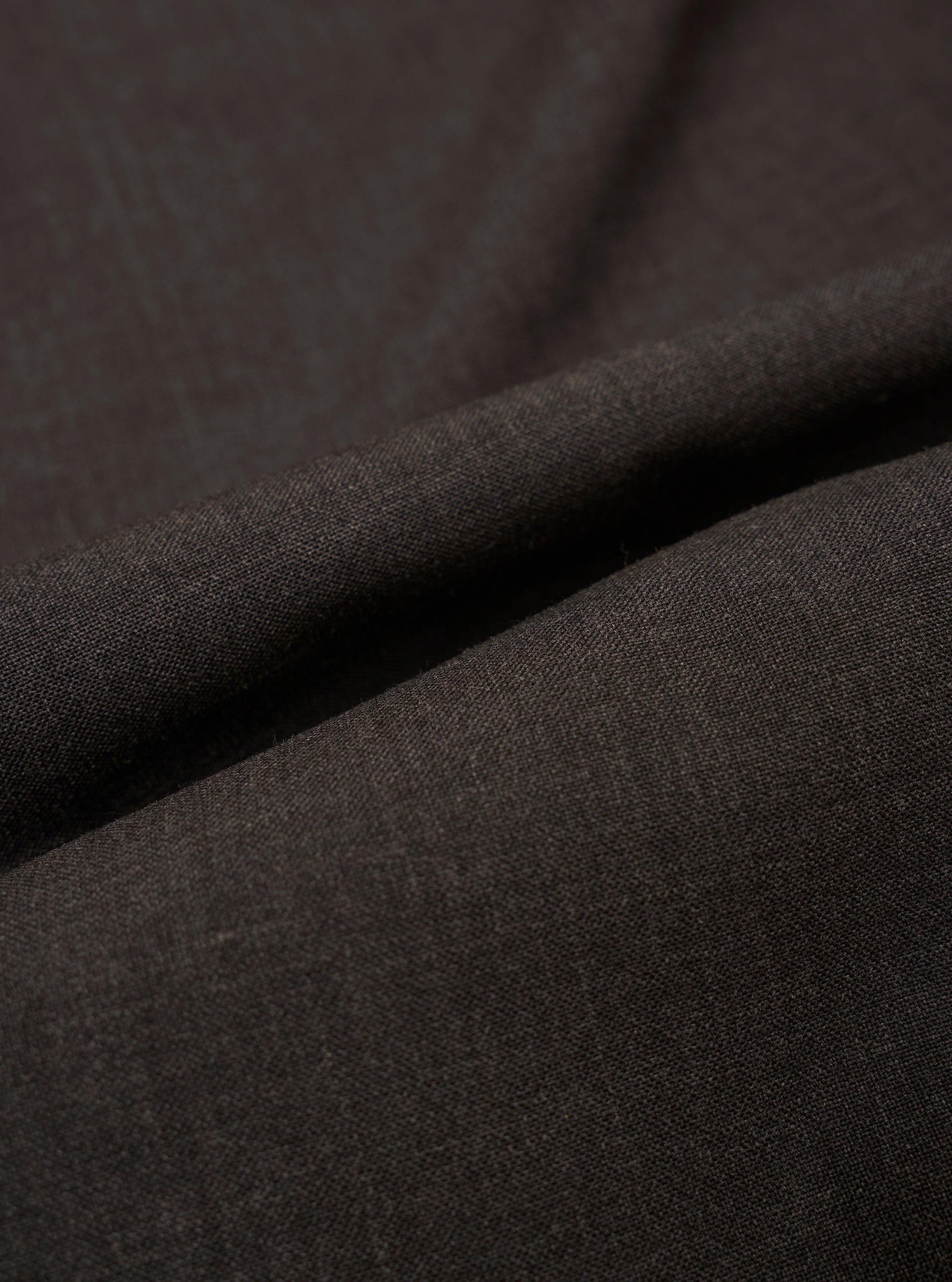 A close-up fabric swatch of the Brown Marl Tropical Suiting Pleated Track Pant shows a detailed view of the marled brown wool-blend material. The image highlights the fine, multi-tonal weave and smooth texture of the tropical suiting fabric.